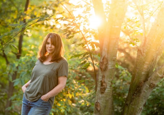 Woman standing with hands in pockets, outside near trees